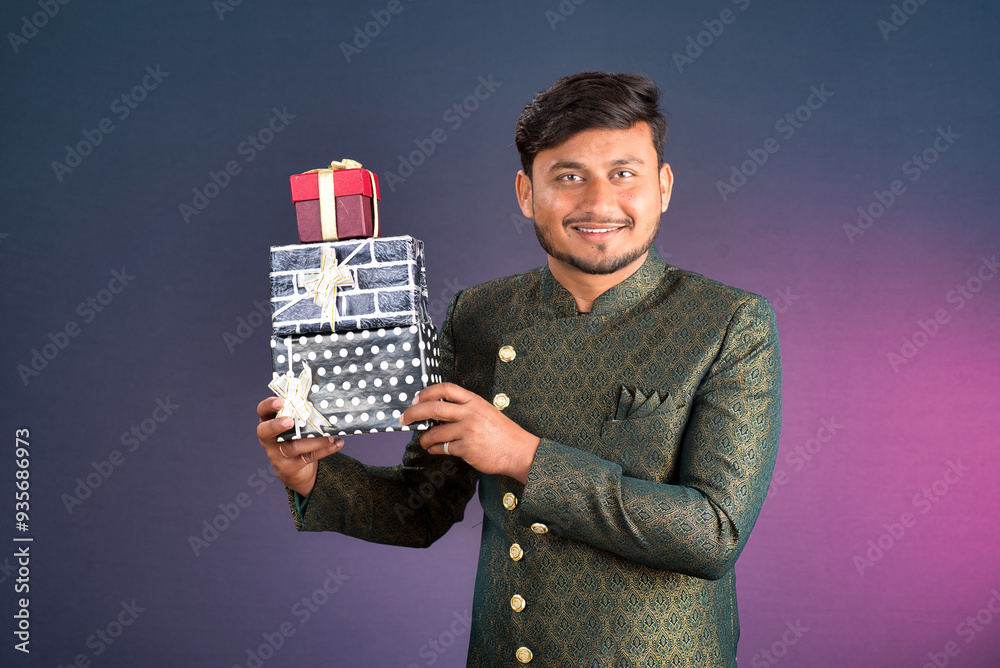 Young happy smiling handsome man holding gift box and posing on dark background Young happy smiling handsome man holding gift box and posing on dark background