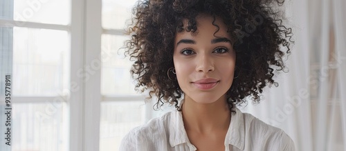 A professional makeup artist and attractive curly haired Latin beauty blogger in a linen shirt explains how to sculpt the body in a home setting with a white interior Copy space The influencer is reco photo