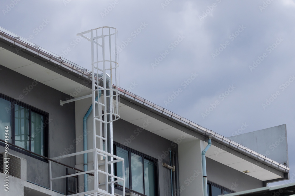 A white ladder on a building with a blue pipe A white ladder on a building with a blue pipe
