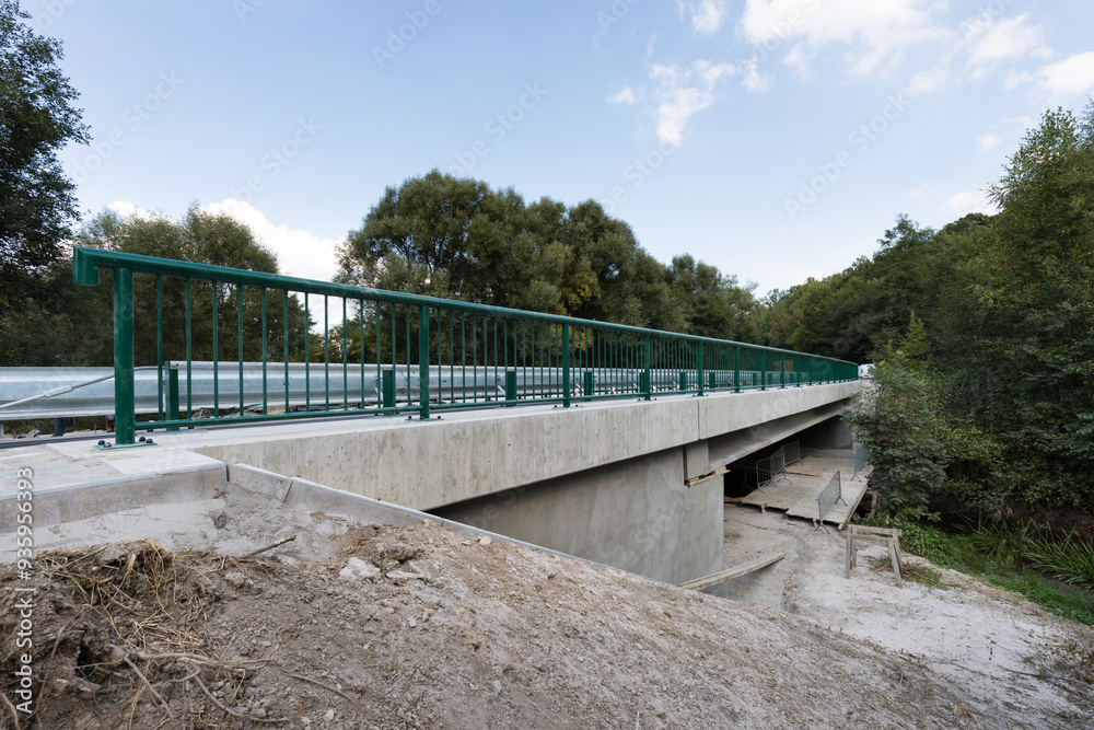 A new modern automobile bridge over the river on the background of the blue sky. A sturdy reinforced concrete bridge, thick concrete pillars and metal floors.
A new modern automobile bridge over the river on the background of the blue sky. A sturdy reinforced concrete bridge, thick concrete pillars and metal floors.