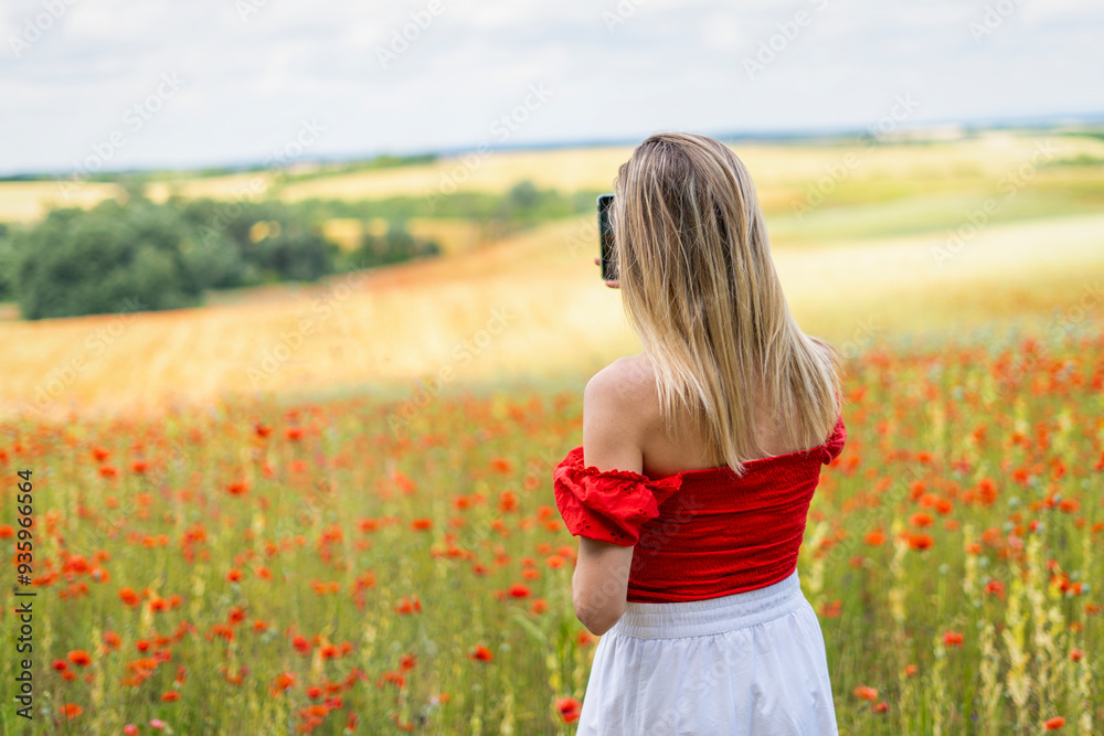 Blonde young woman takes a photo with a phone in a field of red poppies Blonde young woman takes a photo with a phone in a field of red poppies