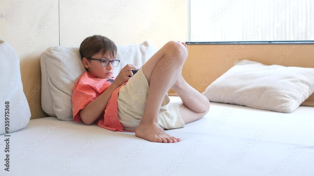 Young boy wearing glasses playing video games while laying on stomach Young boy wearing glasses playing video games while laying on stomach