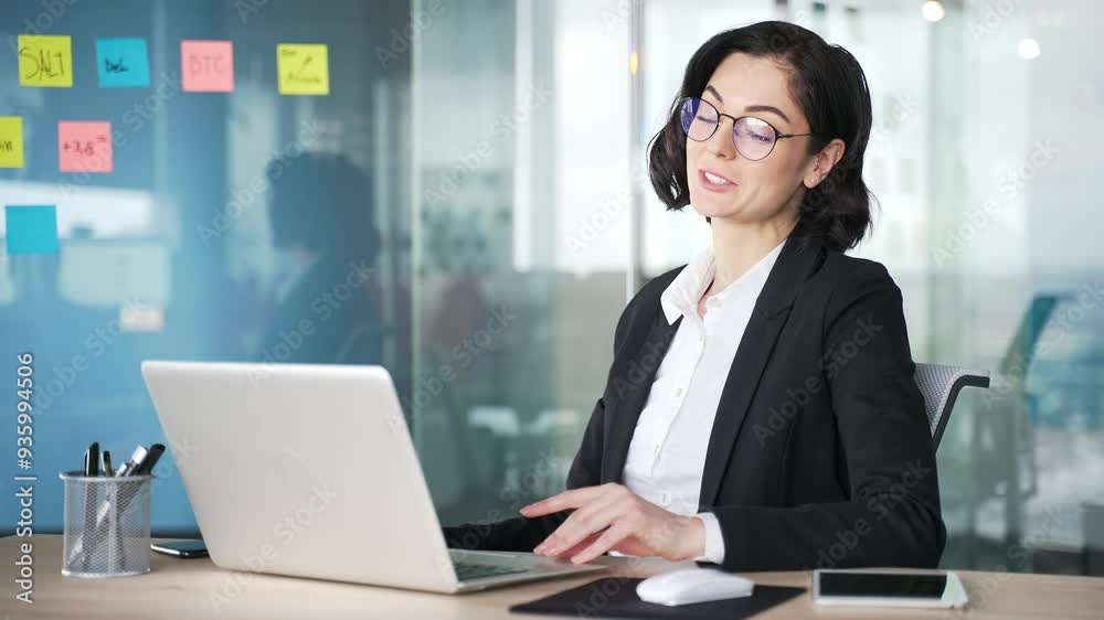 Female professional in business outfit at office desk engaged in a video call using laptop. Communicates through video conference, expressing ideas with hand gestures, displaying remote work setup Female professional in business outfit at office desk engaged in a video call using laptop. Communicates through video conference, expressing ideas with hand gestures, displaying remote work setup