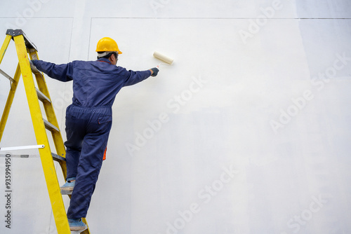Slika na platnu A painter of a newly built house, A painter holding a paint roller skillfully paints a house