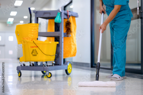 A close-up of mop mopping floor cleaning in office with cleaning cart and floor cleaning tools and equipment using mop cleaning from epoxy floor