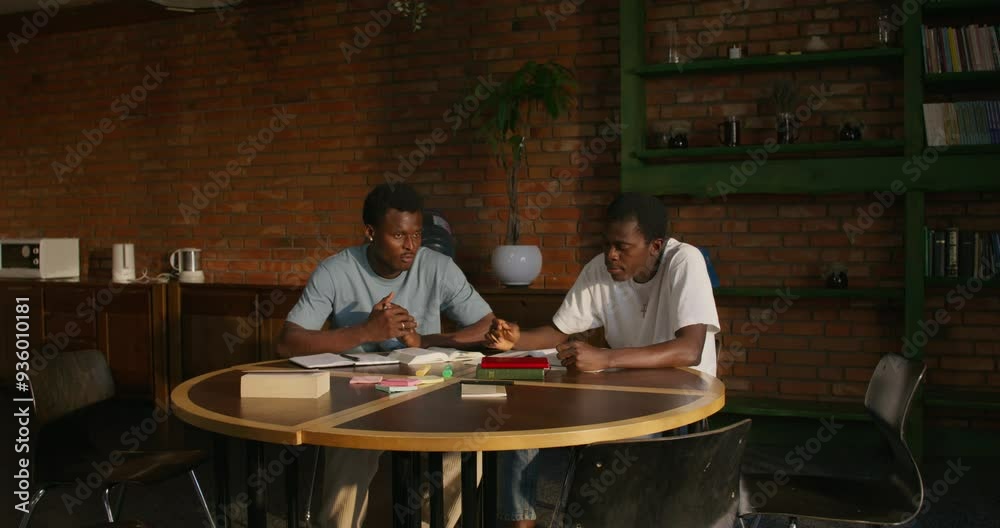 Two men are talking while studying the Bible together. They are sitting at the table indoors Two men are talking while studying the Bible together. They are sitting at the table indoors