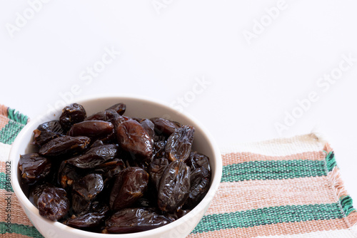 White ceramic bowl filled with dried dates on top of a striped placemat