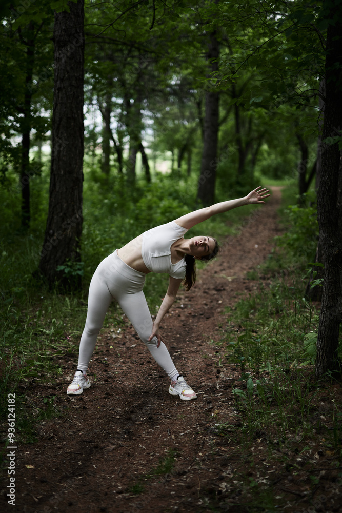 Young caucasian woman in white sportswear exercising in green forest park Young caucasian woman in white sportswear exercising in green forest park