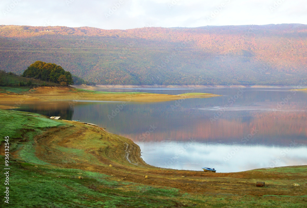 The shore of Rama Lake at sunset. Outdoor recreation in Bosnia and Herzegovina: a deserted winding shore, a mountain colored by the setting sun and the waters of Ramsko jezero with reflections. The shore of Rama Lake at sunset. Outdoor recreation in Bosnia and Herzegovina: a deserted winding shore, a mountain colored by the setting sun and the waters of Ramsko jezero with reflections.