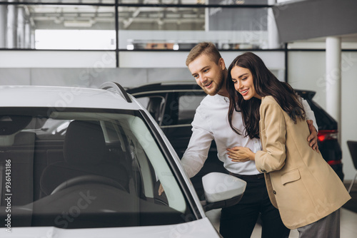 It is the one car I want! Beautiful young couple standing at the dealership choosing the car to buy