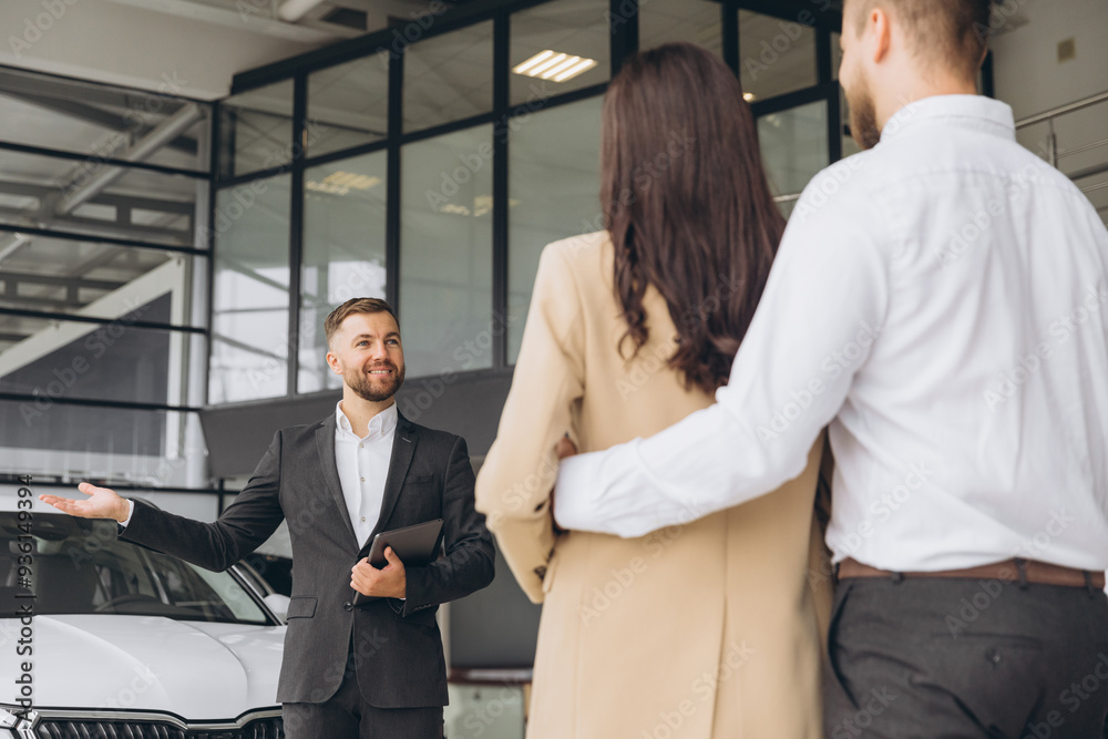 Portrait Of Handsome Car Salesman In Suit Posing At Workplace In Auto Showroom, Young Dealership Center Manager With Clipboard In Hands Helping Spouses To Purchase New Automobile, Free Space Portrait Of Handsome Car Salesman In Suit Posing At Workplace In Auto Showroom, Young Dealership Center Manager With Clipboard In Hands Helping Spouses To Purchase New Automobile, Free Space