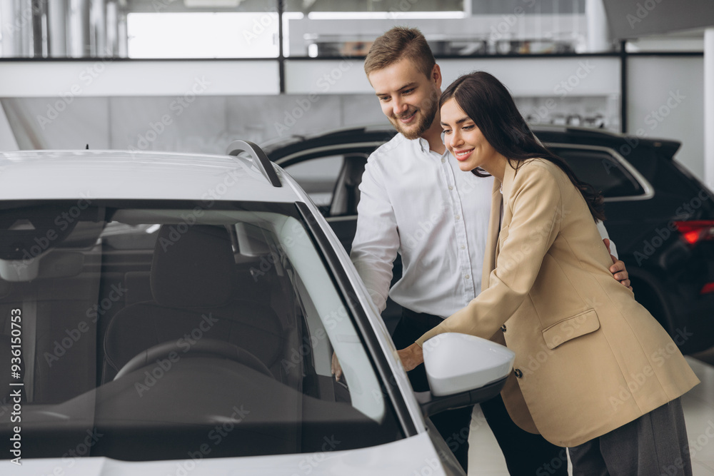 Happy young lovely couple in casual wear hugging while buying first new family car together in dealership. Man shows car keys in showroom. Happy young lovely couple in casual wear hugging while buying first new family car together in dealership. Man shows car keys in showroom.