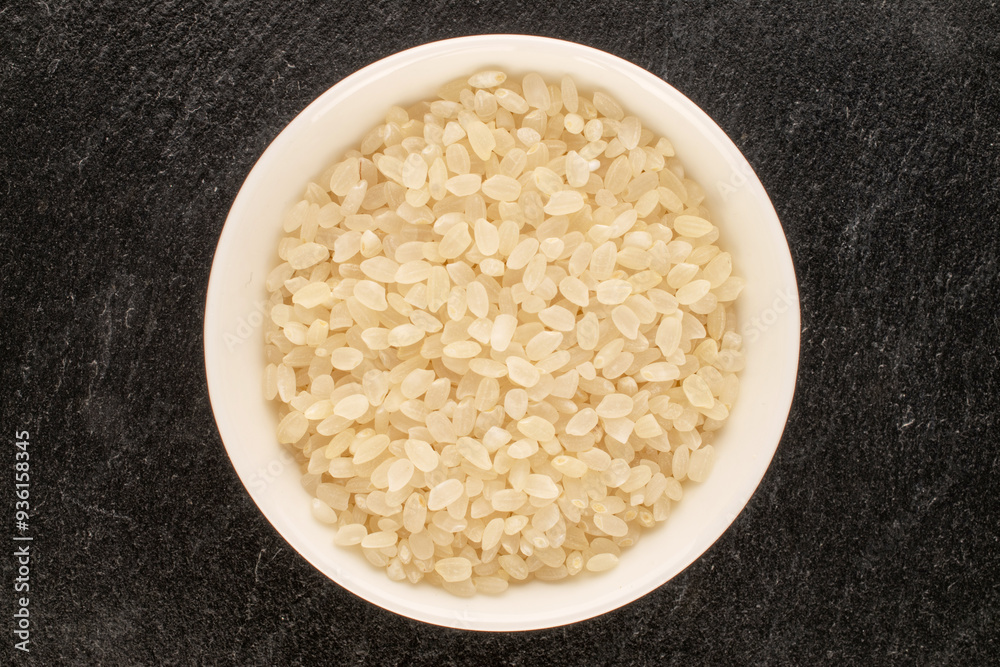 Round grain uncooked rice with white ceramic saucer on slate stone, macro, top view. Round grain uncooked rice with white ceramic saucer on slate stone, macro, top view.