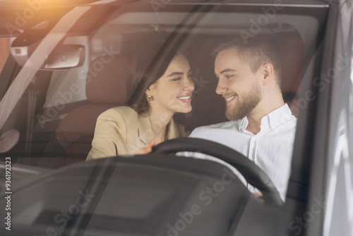 Portrait of smiling beautiful couple sitting in modern luxury car, happy excited young man and woman buying new car in dealership.