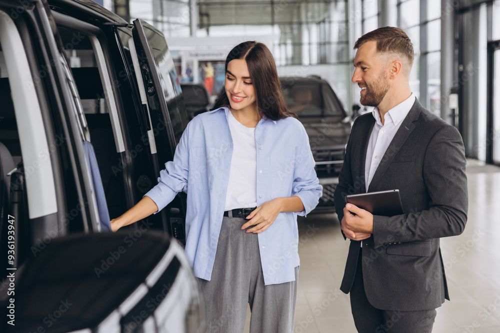 Car Sales Manager Showing Auto Minivan To Caucasian Lady Buyer Standing In Luxury Automobile Dealership Store. Buying Vehicle Concept Car Sales Manager Showing Auto Minivan To Caucasian Lady Buyer Standing In Luxury Automobile Dealership Store. Buying Vehicle Concept