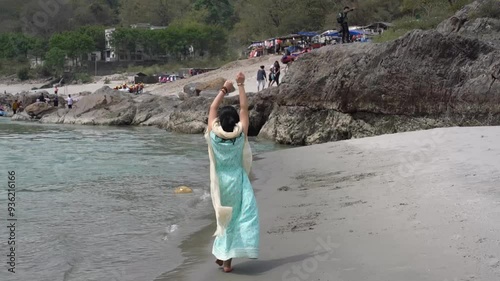 A girl in a blue dress walks on the beach near the Ganges. Rishikesh, India.