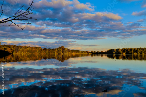 Cloudy sky over autumn forest reflected in the surface of the lake during sunset