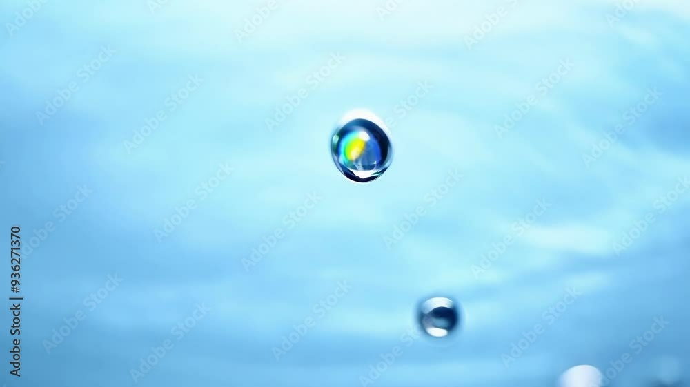 Macro image of water droplets creating concentric circles and splashing on a blue water surface with a blurry background