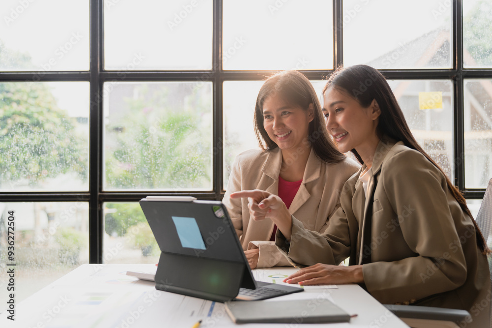 Two young Asian business women Happily sit in the office discussing work using a laptop computer. Two young Asian business women Happily sit in the office discussing work using a laptop computer.
