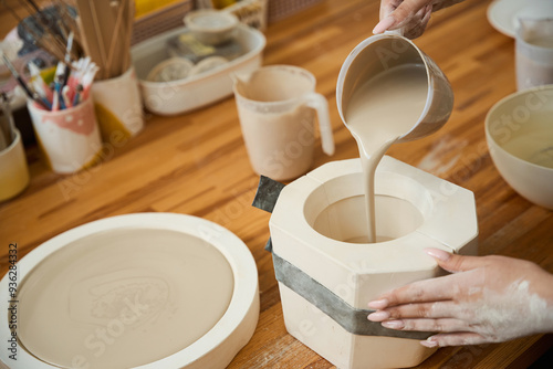 Close up of female hands pouring pottery mixture into mold for mug photo