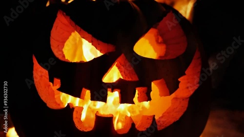 Frightening carved Halloween pumpkin engulfed in fiery flames. The large jack-o'-lantern has a menacing face with glowing eyes.