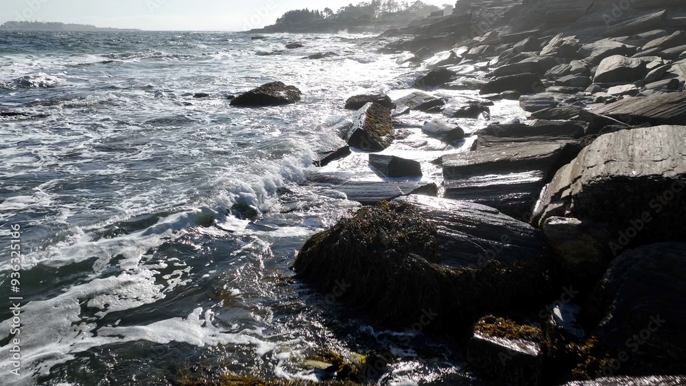 Ocean waves and surf breaking on peaceful rocky coastline beach as sunshine reflects on water during summertime along seashore in Maine Ocean waves and surf breaking on peaceful rocky coastline beach as sunshine reflects on water during summertime along seashore in Maine