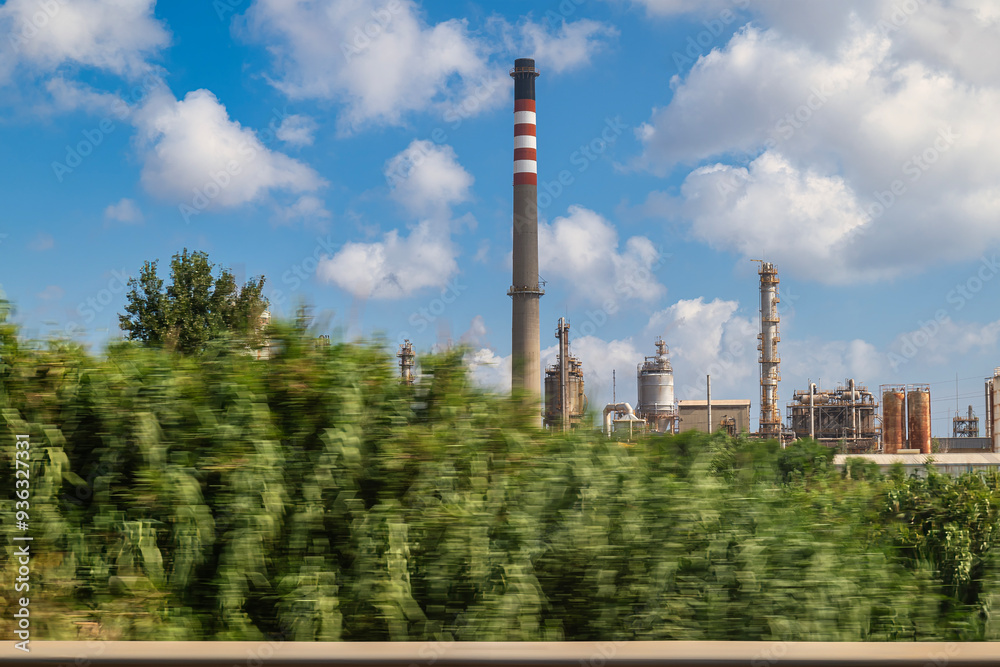Naklejka premium Snapshot taken from a car of an oil refinery amidst vegetation and a cloudy sky