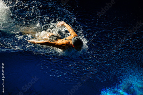 Female athlete swims with a butterfly style. Splashes of water scatter in different directions