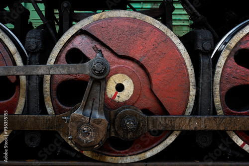 Large red iron wheel and mechanism of an old steam locomotive.