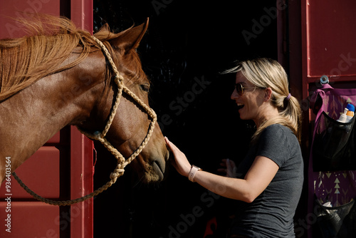 Woman with sorrel mare horse at trailer in halter, western lifestyle on ranch, happy person