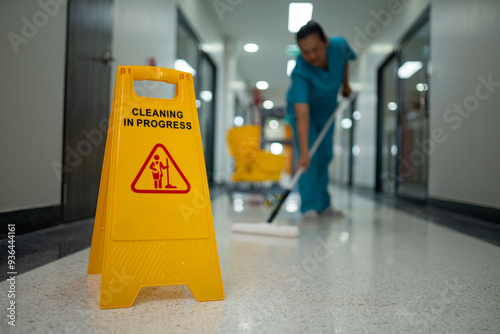 A woman is cleaning a floor with a yellow sign that says 