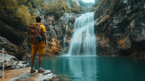 Fototapeta Naklejka Na Ścianę i Meble -  Hiker admiring a serene waterfall in a lush forest during autumn