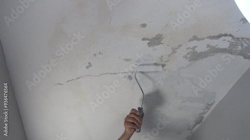 Close up view of craftsman painting damaged leaky ceiling roof with a paint roller.