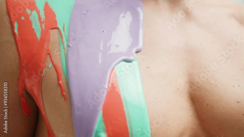 Colourful paint flowing over the man body close-up. Body art therapy with many various of paints. Painting on human body.