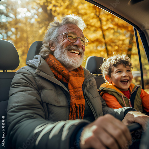 elderly man around 70 years old, with grey hair, drives a car. In the backseat young child. The car travels down a road lined with autumn trees