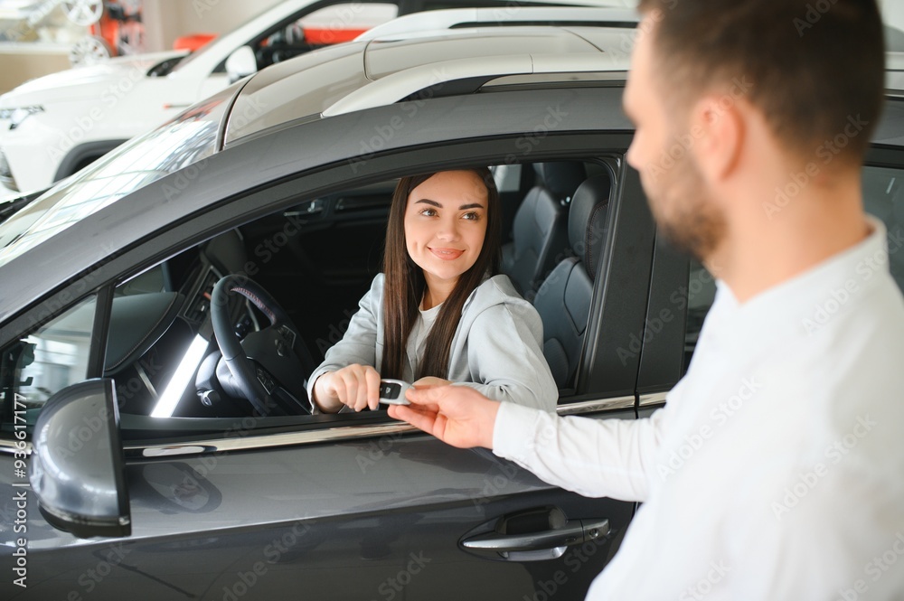 Dealer giving key to cheerful female driver while selling modern red vehicle in dealership Dealer giving key to cheerful female driver while selling modern red vehicle in dealership