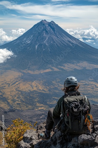 Hiker gazes at a majestic volcano from a rocky peak on a sunny day