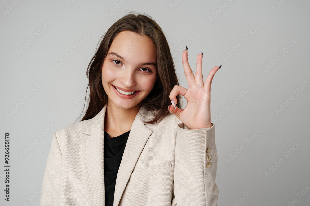 Young Woman With Brown Hair Making the Ok Sign in a White Sweater Against a Grey Background Young Woman With Brown Hair Making the Ok Sign in a White Sweater Against a Grey Background