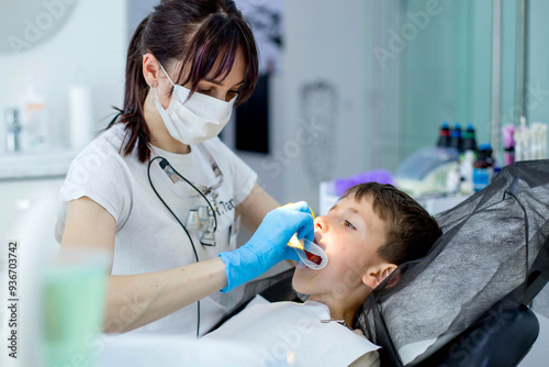 Fotografie Paediatric dentist putting a cheek retractor on child patient before dental trea