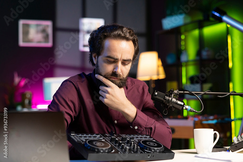 Artist filming DJ mixing tutorial, thinking of examples of sampling on sound controller to teach audience. Man contemplating if mixer musical equipment deserves endorsement photo