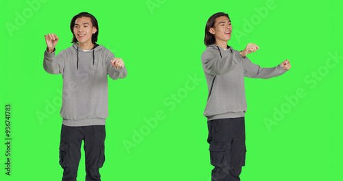 Asian guy acting as choir conductor for musical show, moving hands like a bandmaster director over greenscreen backdrop. Male model conducting band to sing, smiling choirmaster. photo