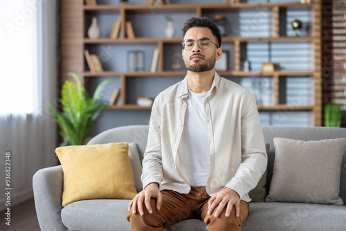 фотографія Young man meditating with closed eyes on a comfortable sofa at home, focusing on