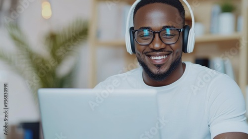 A man wearing glasses and headphones is smiling while looking at a laptop