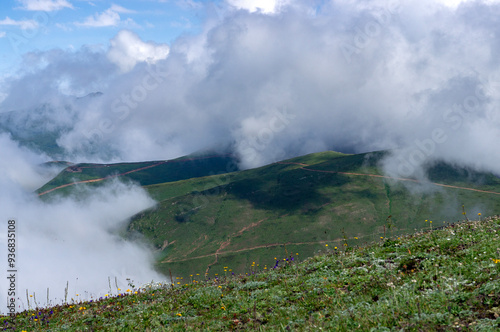 Green summer mountains, beautiful hills covered in green grass. Big fluffy clouds, or fog, over the mountains. Hiking season.