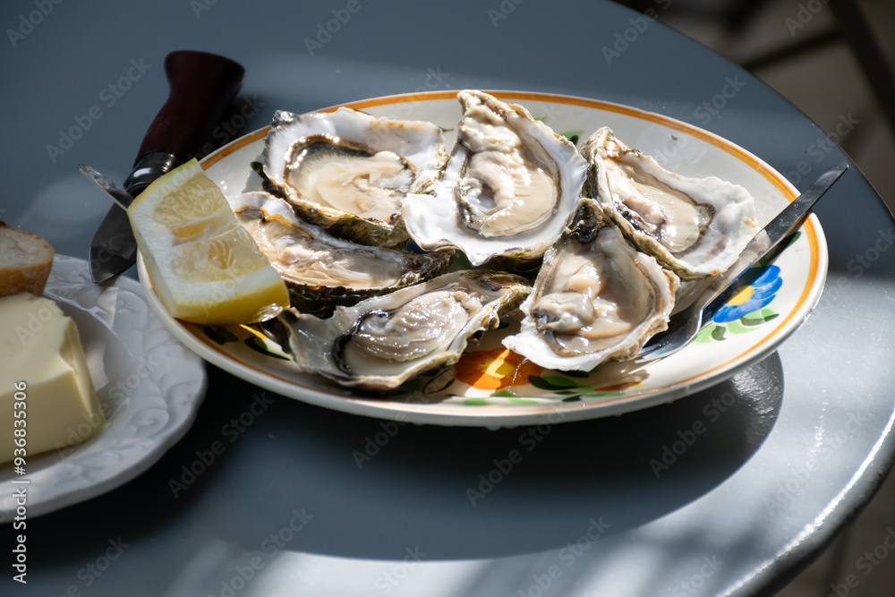 Plate with fresh live oysters with citron, bread, butter and white wine served at restaurant in oyster-farming village, Arcachon bay, Gujan-Mestras port, France