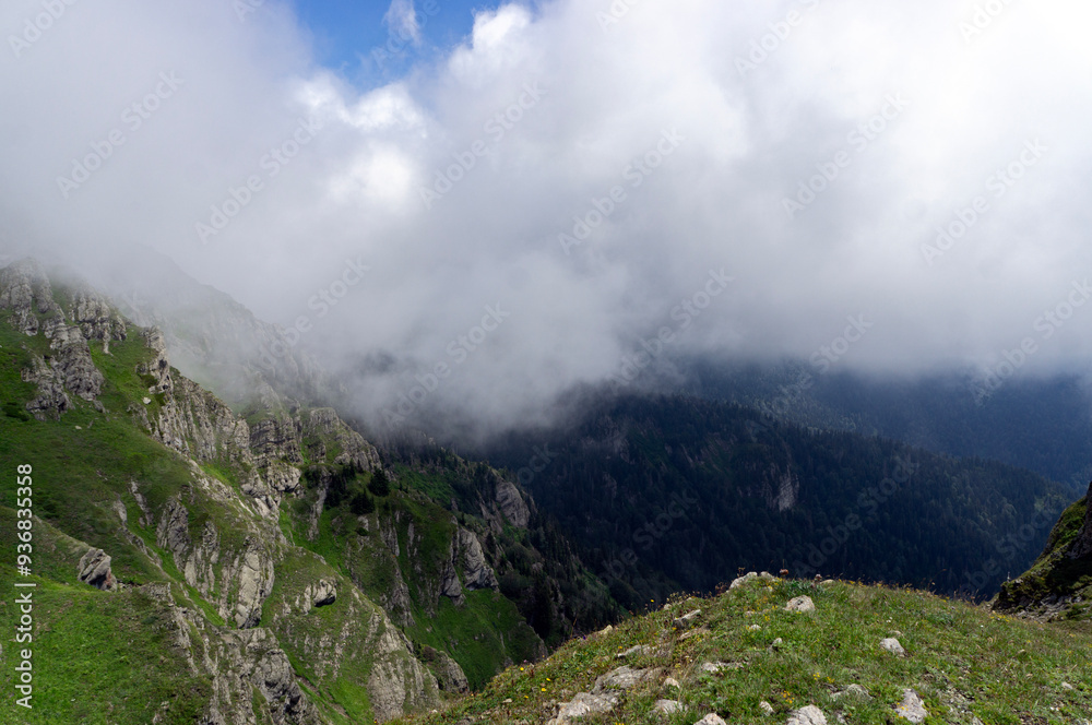 Fototapeta premium Green summer mountains, beautiful hills covered in green grass. Big fluffy clouds, or fog, over the mountains. Hiking season.
