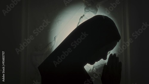 Side view of silhouette of nun in monastic hood praying to Lord, low key backlighting
