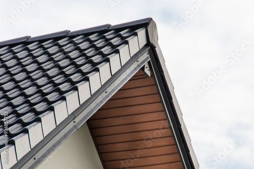 Modern Architectural Detail of a Roof Featuring Stylish Tiles and Wooden Eaves Against a Bright Sky