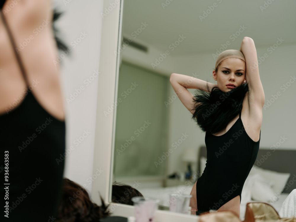 Woman in black leotard fixing hair in front of mirror, preparing for performance with focused expression Woman in black leotard fixing hair in front of mirror, preparing for performance with focused expression