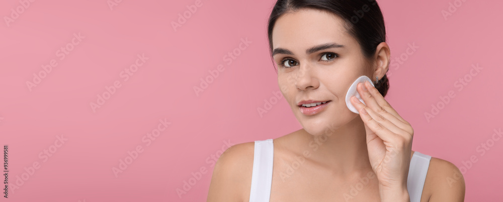 Young woman cleaning her face with cotton pad on pink background. Banner design with space for text Young woman cleaning her face with cotton pad on pink background. Banner design with space for text